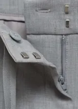 Pantalón largo de tiro medio color gris, estilo jogger, con dos bolsillos laterales, cierre oculto de botón, gancho y cremallera, y forro interior.