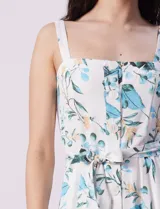 Vestido midi blanco con estampado floral celeste y verde, escote recto con tirantes, abertura frontal con botones, lazo en la cintura y bolsillos laterales.