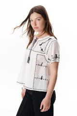 Blusa negra con bordados blancos de animales y motivos geométricos. Tiene cuello redondo con lazo y mangas cortas.