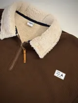 Buzo marrón de pana con cuello tipo polo con forro de corderito blanco, cierre parcial con cremallera y bolsillo tipo canguro.