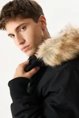 Campera negra con capucha con borde de piel sintética color beige, cierre frontal con cremallera y botones a presión, bolsillos laterales con solapa y puños acanalados.