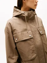 Campera marrón de Tommy Hilfiger con capucha con cordón ajustable, cierre de cremallera oculto con botones a presión, dos bolsillos delanteros tipo sobre con botón, logo metálico en el puño y corte amplio.