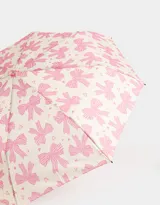 Paraguas corto con estampa de moños y corazones rosas sobre fondo crema, con mango curvo de plástico transparente color rosa.