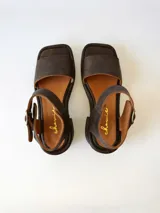 Sandalias de cuero color chocolate, con tira ancha sobre los dedos, pulsera al tobillo con hebilla metálica y taco cuadrado de 6 cm.