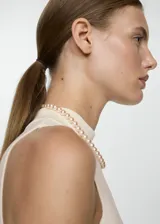 Vestido corto evasé color crudo, de tejido de punto fino, sin mangas y con cuello perkins.