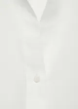 Camisa blanca de algodón con cuello camisero, manga larga con puños abotonados y cierre frontal con botones.