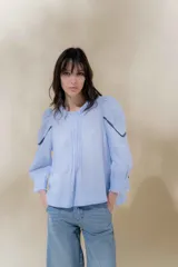 Blusa de lino blanca con escote a la base y terminación de voladito al bies desflecado. Delantera con alforzas verticales y mangas románticas tres cuartos, con detalle de puntilla. Puños con alforzas y voladitos que suman un toque femenino. Espalda abotonada.