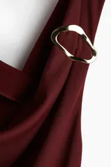 Vestido midi color vino tinto, sin mangas, con escote drapeado tipo cascada y un detalle de argolla metálica plateada en el bretel derecho. Presenta frunces laterales a lo largo del torso.