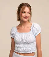 Blusa corta de tricolina a rayas celestes y blancas, con escote elástico, mangas cortas abullonadas con frufrú y fruncido en el bajo.