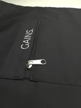 Bolso tipo tote bag negro con asas largas, bolsillo exterior con cierre y bordado con la palabra "GAINS." en blanco.