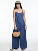 Mono de denim azul de lyocell, con breteles finos regulables que se cruzan en la espalda. Tiene bolsillos traseros y corte amplio de pierna recta.