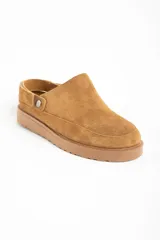 Zueco tipo mule de gamuza color camel, con forro interior de corderito visible en el borde. Presenta una tira ajustable con broche metálico en el lateral y suela de goma gruesa y dentada.