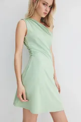 Minivestido verde de punto elástico, con escote asimétrico de un hombro, manga corta con detalle girado y frunces laterales que crean un efecto drapeado suave.