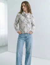 Buzo de tejido de punto con cuello vuelto que se ajusta con botones. Presenta un diseño jacquard en tonos blanco, gris y rosado pálido.