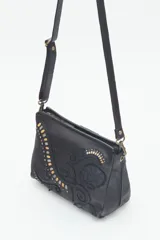 Cartera bandolera verde de cuero vacuno con bordado de flores y tachas doradas y plateadas. Tiene cierre metálico superior, forro de algodón, división interna, bolsillo y tarjetero. La correa es regulable.