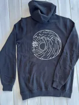 Hoodie negro con capucha y cordones ajustables. Estampado en la espalda con un diseño circular que incluye una ola, un sol y una palmera.