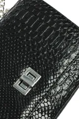 Bandolera negra con textura de piel de serpiente, solapa frontal y cierre metálico plateado. Cuenta con una correa de cadena plateada.