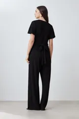 Mono largo negro con textura plisada, escote cruzado en V, mangas cortas con volados y pantalón palazzo.