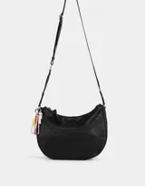 Bandolera hobo negra de tela deportiva con correa regulable, cierre superior, bolsillo frontal y charm lateral decorativo.