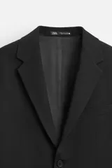 Blazer slim fit negra confeccionada en tejido con viscosa. Cuello con solapas de muesca, manga larga con puño con detalle de botones, bolsillo de vivo en pecho y de solapa en cadera, bolsillo interior, bajo con aberturas en espalda y cierre frontal con botones.