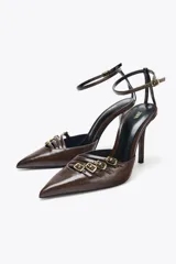 Zapato de tacón destalonado color marrón, con punta fina, tiras frontales con hebillas metálicas y pulsera al tobillo con cierre de hebilla.