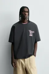 Camiseta negra de corte holgado con cuello redondo y mangas cortas. Estampado frontal y trasero con textos y figuras en color rosa.