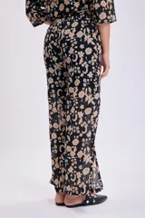 Pantalón de corte palazzo con estampado floral en tonos beige sobre fondo negro.