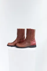 Botas de media caña color marrón de cuero vacuno, con detalle de costuras en la capellada y contrafuerte color bordó. Suela de caucho con taco bajo.