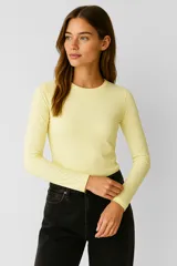 Remera de poliéster color amarillo claro, de manga larga, corte ajustado y cuello redondo.