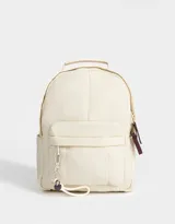 Mochila color crema de tela acolchada con pespuntes verticales. Tiene un bolsillo frontal con cierre, doble cierre superior, manija superior, correas regulables y bolsillos laterales. Incluye un charm colgante de corazón.
