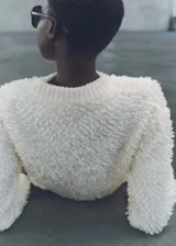 Sweater de punto grueso color blanco con terminaciones de canalé, cuello redondo y tejido bouclé.