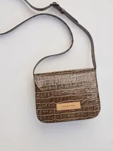 Cartera bandolera marrón con textura tipo piel de cocodrilo, solapa con cierre imantado y correa fina regulable.