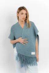 Ruana celeste tejida a mano en cinta de lana merino, con flecos en el borde inferior.