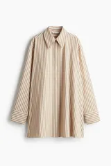 Camisa oversized de sarga color beige con rayas verticales marrones, cuello clásico, cierre frontal con botones ocultos, mangas largas con puños abotonados y bajo recto.