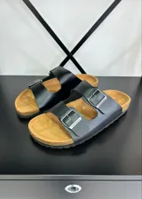 Sandalias negras con plantilla color suela y dos tiras anchas con hebilla metálica ajustable.