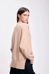 Cardigan de punto color beige con corte lateral, escote en V, cierre con botones y bolsillos frontales.