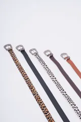 Cinturón de estilo western con hebilla metálica plateada ornamentada. Disponible en varios colores y estampados: cuero marrón claro, cuero marrón oscuro, estampado dálmata (blanco y negro) y cuero negro liso. También disponible en estampado leopardo.