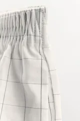 Shorts de algodón color gris claro con estampado de cuadros negros, tiro medio y cintura elástica.