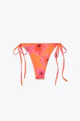 Braguita de bikini estampada con flores rojas y anaranjadas sobre fondo naranja. Tiene tiro medio y cintura ajustable con lazadas.