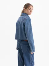 Camisa de denim azul de manga larga, corte cuadrado y silueta corta. Presenta un bordado integral en patrón de rombos con detalles en rosa y bordeaux.
