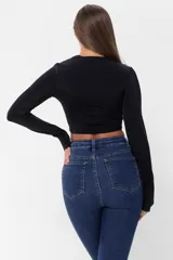 Top negro de lycra con manga larga y corte irregular con aberturas en el escote y detalle de hebilla metálica.