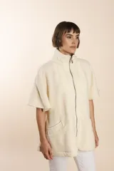Capa acampanada color beige con manga corta, cierre metálico a la vista, cuello recto, bolsillos con tapa y terminaciones envivadas. Confeccionada en lana fina sin teñir, diseñada exclusivamente por Don Baez.