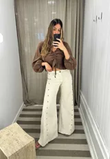 Pantalón de jean color crudo, corte palazzo, con tachas metálicas en los laterales y ruedo desflecado.