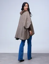 Ruana de tejido suave, color beige y marrón con estampado geométrico repetitivo. Posee cuello con aplique de piel sintética marrón y ribetes negros. Se combina con un suéter marrón de manga larga con botones en el puño.