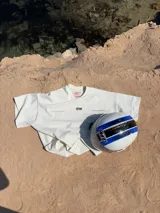 Remera color crema de corte recto y mangas cortas, con estampado en la espalda con el logo "ITTAI" en negro con líneas rojas, azules y blancas, y la leyenda "AN IBIZA PRODUCE. Ittai Stars Department Gallery - Ibiza Edition. If you're in Ibiza, 112 is not an option.".