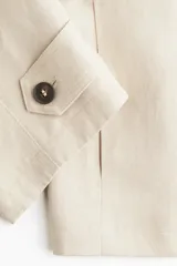 Chaqueta corta color beige, de corte oversized, con cuello clásico, charreteras abotonadas, bolsillos laterales y trabilla con botón en los puños.