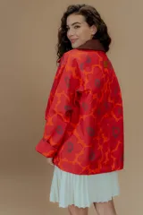 Campera tipo parka reversible con estampado de flores rojas y naranjas sobre fondo rojo, cuello marrón y bolsillos frontales.