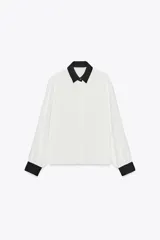 Camisa blanca de manga larga con cuello y puños negros. Cierre frontal con botones.