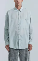 Camisa celeste de manga larga con bolsillo con ojal y botón en el delantero, de calce oversize confeccionada en textil plano fresco y liviano.