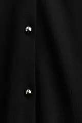 Chaleco corto de punto negro con cuello redondo y botones metálicos.